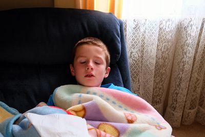 Boy sleeping on chair by window at home