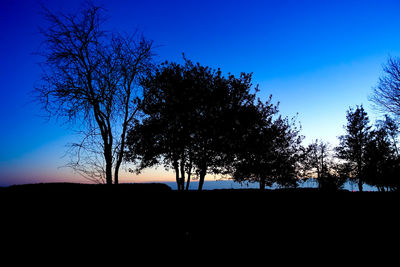 Silhouette trees on field against clear blue sky