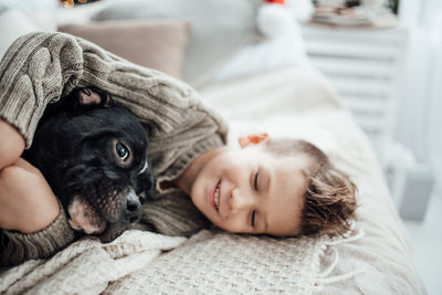 Cute smiling boy relaxing on bed with dog at home
