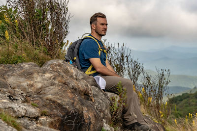 Man sitting on rock against sky