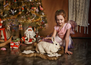 Cute girl with rabbit by christmas tree at home