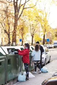 Male with female environmentalist throwing plastic bottles in garbage can