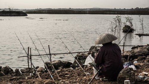 Rear view of fisherman with fishing rods by lake