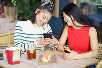 Smiling friends using mobile phone while sitting at restaurant