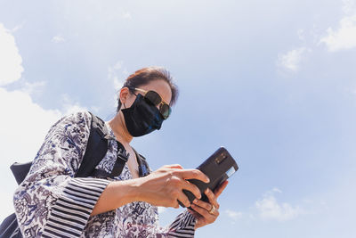Low angle view of woman holding mobile phone against sky