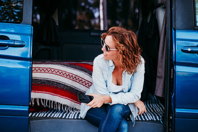 Woman wearing sunglasses holding mobile phone while sitting in camper trailer