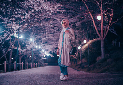 Portrait of woman standing by trees at night