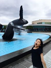 Portrait of girl screaming by fountain against sky