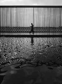 Side view of silhouette man walking by lake with fence reflection