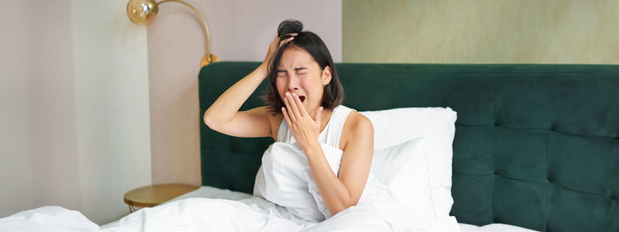 Portrait of young woman sitting on bed at home