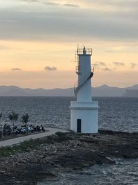 Lighthouse by sea against sky during sunset