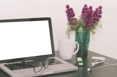 Laptop with eyeglasses by flower vase on table