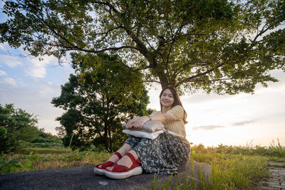 Portrait of young woman sitting on plant against trees