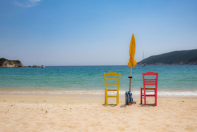 Two empty colourful chairs and a yellow umbrella on a beach