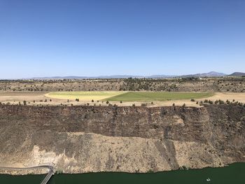 Scenic view of bridge, river, cliffs, and farmland against clear blue sky