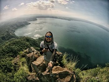 High angle view of man holding monopod while standing on rock against sea