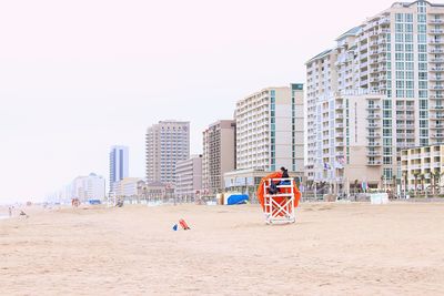 People on beach against buildings in city against clear sky