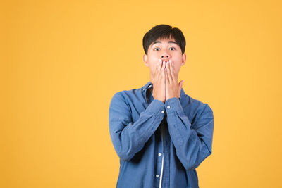 Portrait of young man standing against yellow background