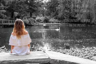 Rear view of woman sitting by lake against trees