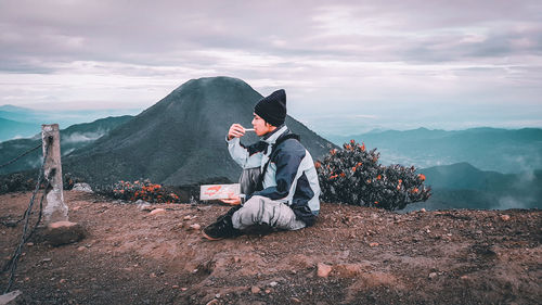 Man sitting on mountain against sky