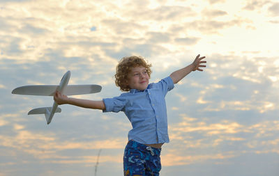Boy holding toy airplane against sky during sunset