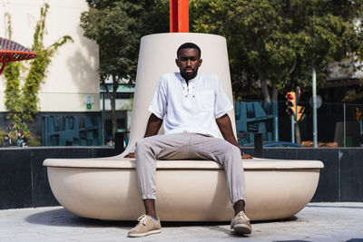 Confident african american male in summer outfit relaxing on concrete bench in city on sunny day