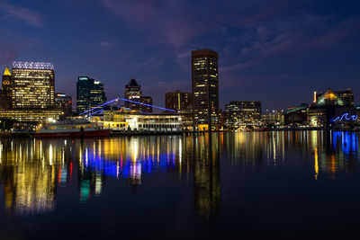 Illuminated buildings by river against sky at night