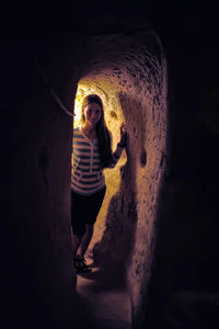 Portrait of young woman standing against dark wall