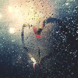 Person holding umbrella seen through wet glass window