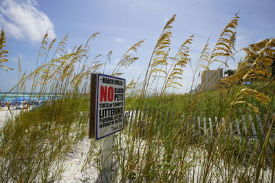 Information sign on grass at beach against sky