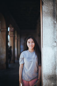 Portrait of smiling young woman standing in corridor of building