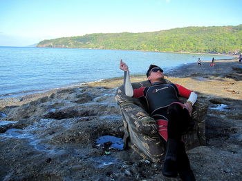 Rear view of woman sitting on rocks at beach