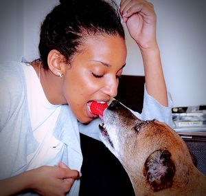 Close-up of young woman eating strawberry with dog at home