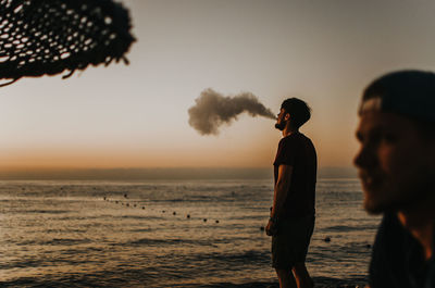 Man standing at beach against sky during sunset