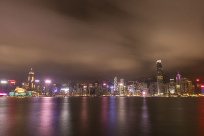 Illuminated buildings by river against sky at night