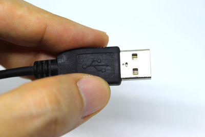 Close-up of person holding usb cable against white background