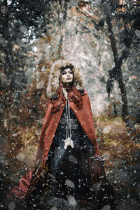 Young woman wearing cape during snowfall in forest