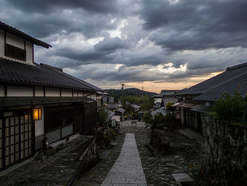 Footpath amidst houses and buildings against sky at sunset