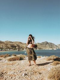 Young woman standing at beach against clear sky