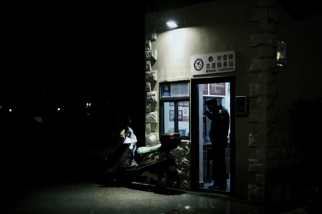 night, illuminated, architecture, built structure, building exterior, one person, text, store, communication, real people, city, sign, lighting equipment, outdoors, building, full length, sitting, western script