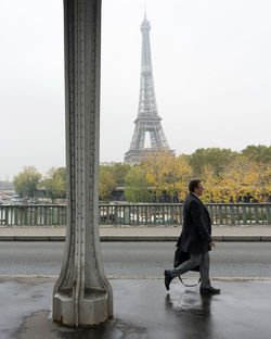 Full length of man walking by eiffel tower in city against sky