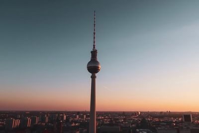 Communications tower in city against clear sky during sunset