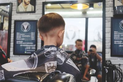 Rear view of boy wearing cape sitting in hair salon