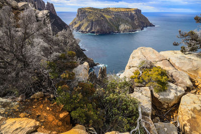 Scenic view of rocks by sea against sky