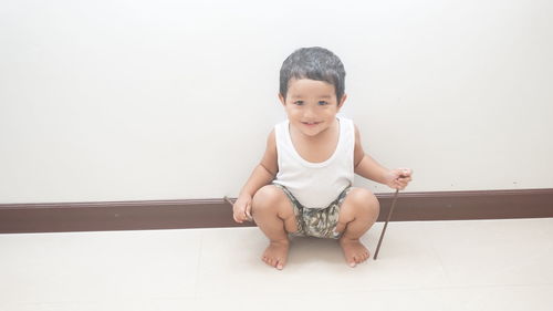 Portrait of cute smiling baby boy crouching against wall at home