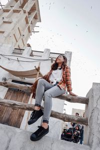 Full length of woman sitting against building in city