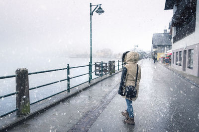 Rear view of woman walking on wet street during winter