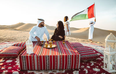 Happy parents with tea on carpet against children with united arab emirate flag sat desert