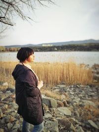 Side view of woman looking away while standing on rocks by lake against sky