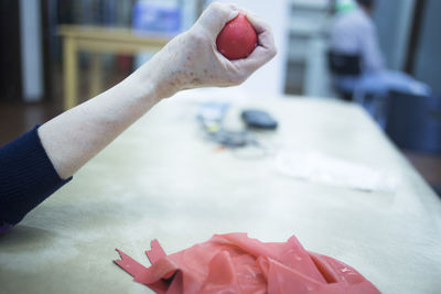 Cropped hand of person holding rubber ball on table